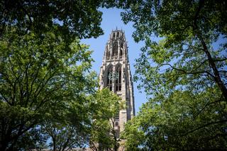 The dramatic and gothic Harkness Tower, as seen through treetops, rises into the vibrant blue sky